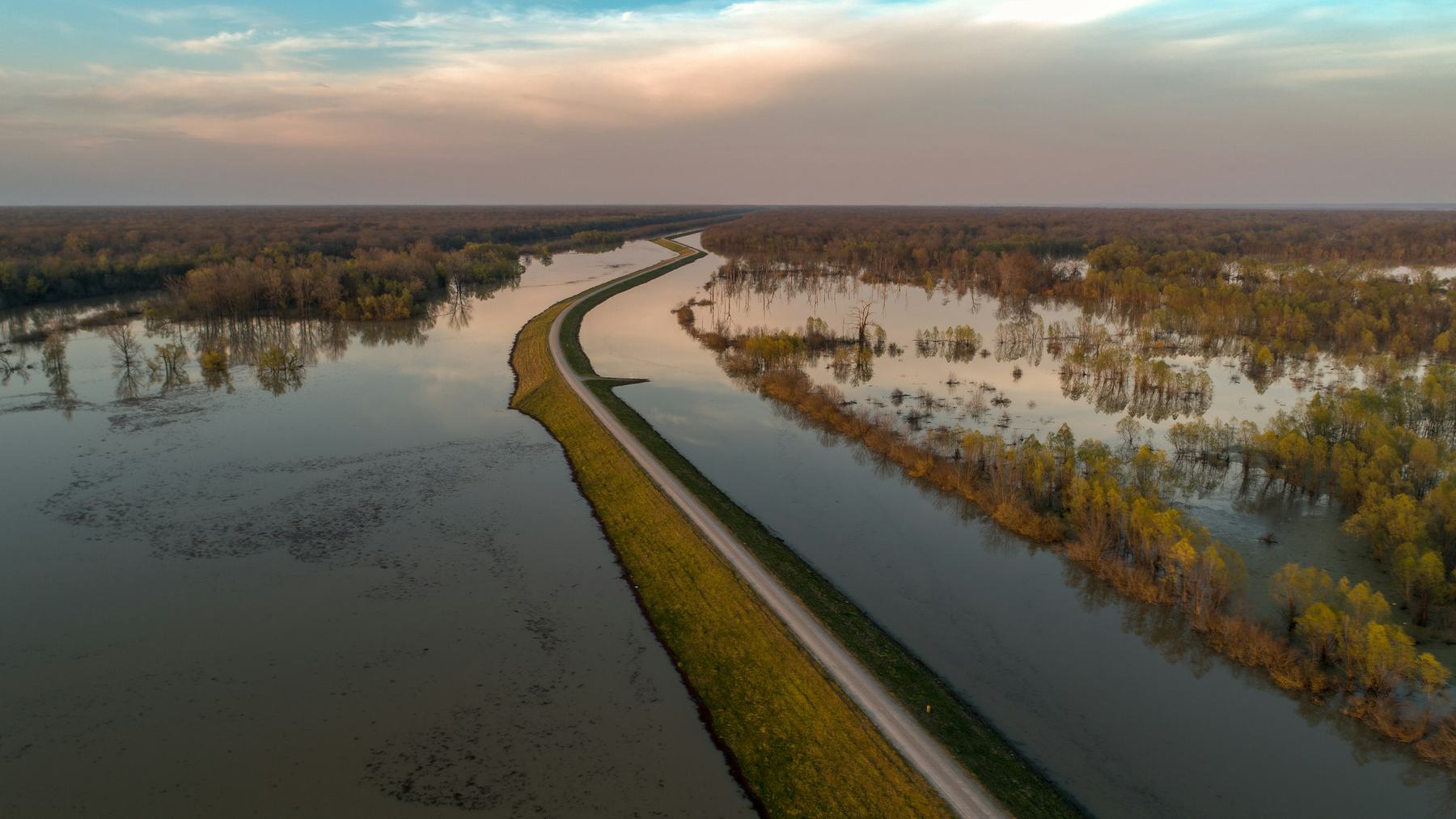 A levee road running through a flooded plain at sunset